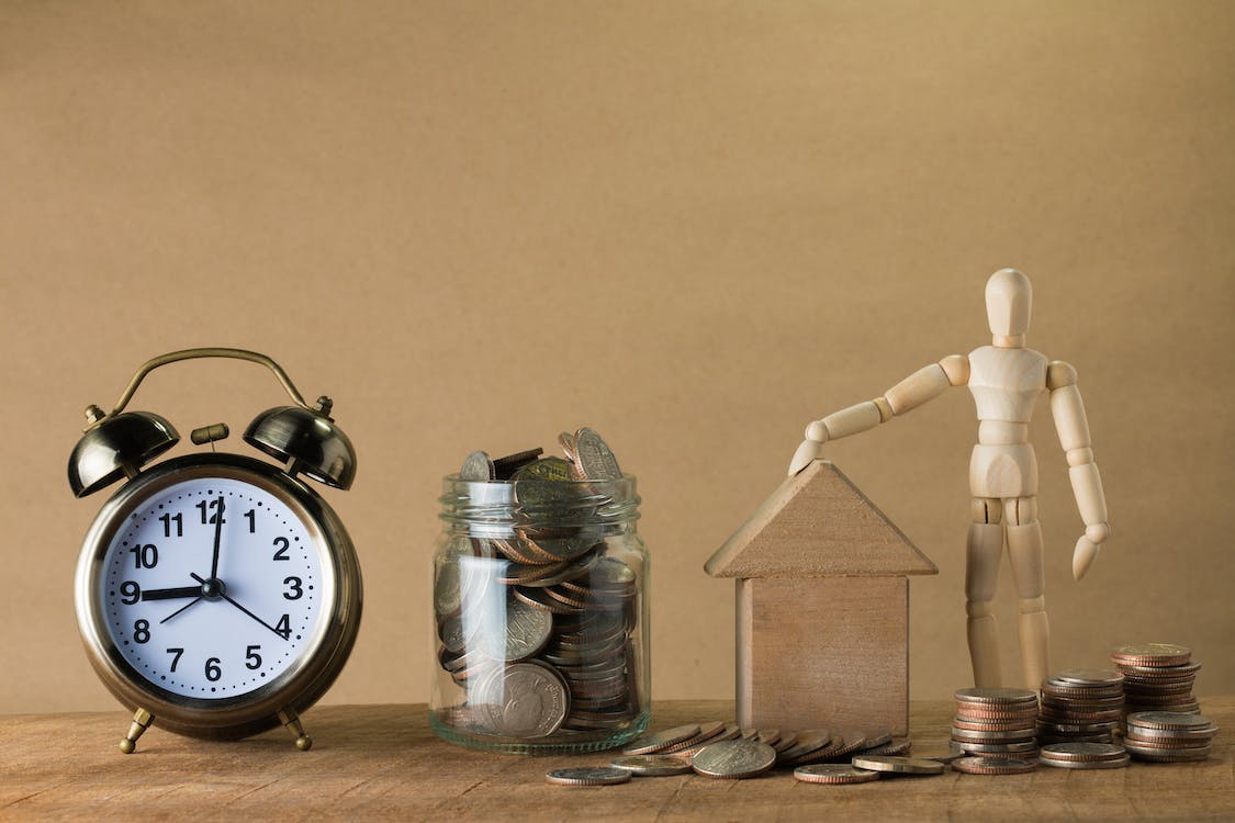 A picture of a clock, a jar filled with money, a wooden house and a wooden puppet.